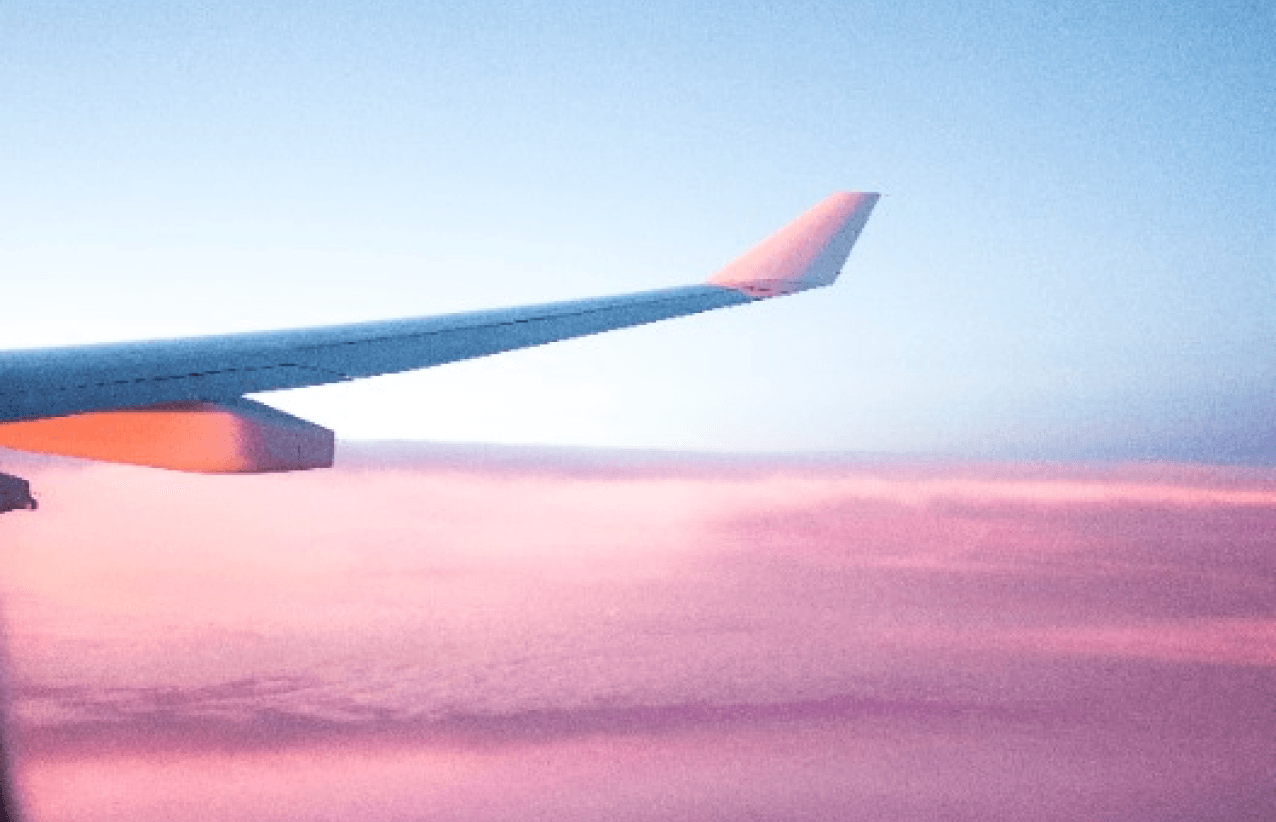 A photo of a pink sky and a plane wing taken from inside the plane.